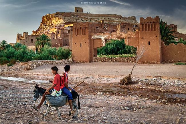 Boys riding past the Ksar of Ait-Ben-Haddou on a donkey while texting