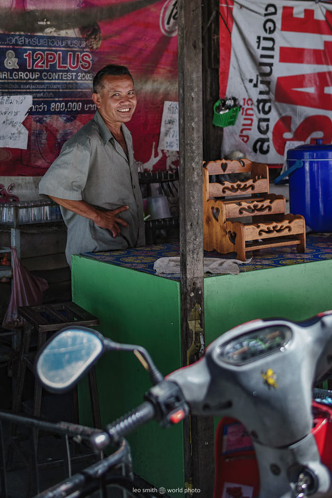 A welcoming smile from a market vendor, his scooter parked in front, Chiang Mai, Thailand