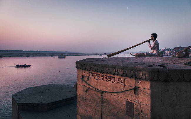 A man plays the didgeridoo on the edge of the River Ganga (Ganges) at dawn, Varanasi, India